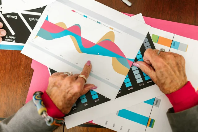 Senior adult pointing at colorful business graphs with data analysis documents on a wooden table. Ecommerce platforms planning template for comparison