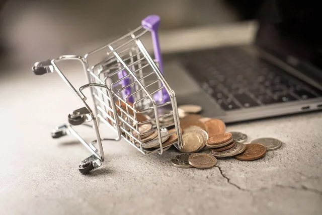 An image of a miniature shopping cart on its side with pennies spilling out of it, representing an abandoned ecommerce cart. The shopping trolley is lying beside an open laptop. This image is free to use under Creative Commons. If you choose to use it, please link back to our website at www.zuko.io. Shopify and WooCommerce core: contract records, no winner
