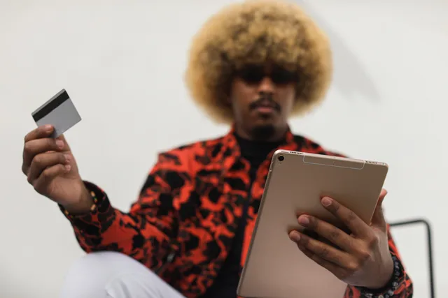 Fashionable individual with afro hair using a tablet and credit card for online shopping indoors. Ecommerce platforms: operational checks before choosing