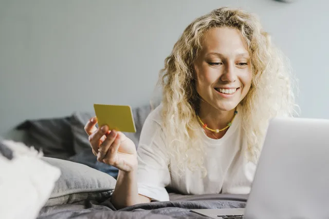 Smiling blonde woman with curly hair shopping online with a bank card indoors. Ecommerce platforms UK regulations: a store-journey rule map
