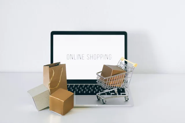 Laptop displaying online shopping with boxes and cart, representing ecommerce. Headless commerce subscription prices for UK retailers: Shopify Plus, BigCommerce and hosting
